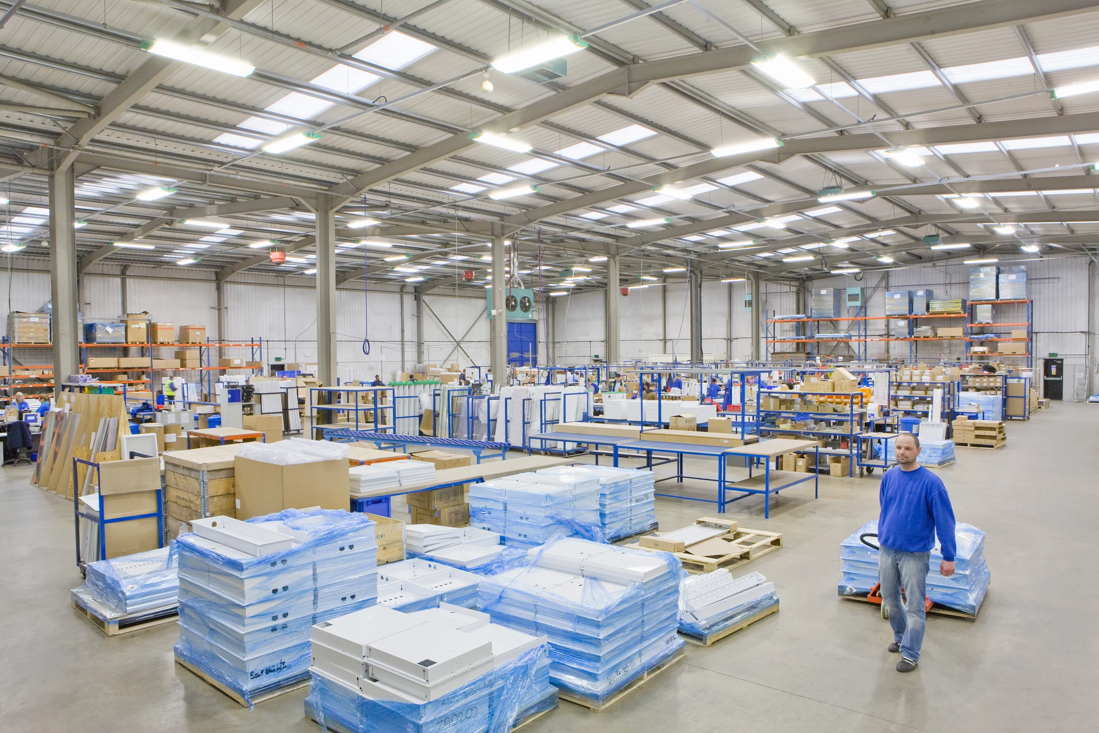 A warehouse worker moving a pallet among stock and packing stations